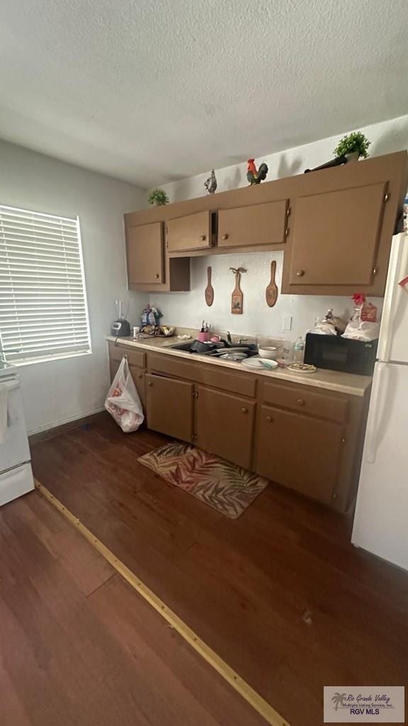 kitchen featuring black microwave, freestanding refrigerator, dark wood-style floors, a textured ceiling, and range