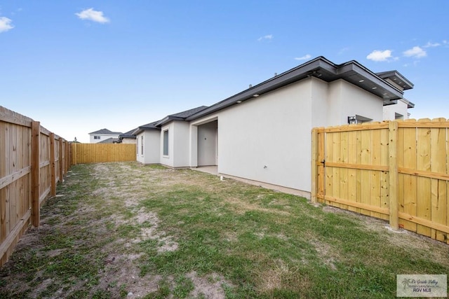 rear view of house featuring a yard, a fenced backyard, and stucco siding