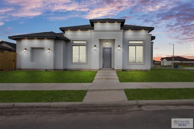 prairie-style house featuring a front lawn, fence, and stucco siding