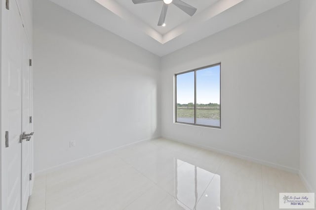 unfurnished room with ceiling fan, baseboards, a tray ceiling, and light tile patterned flooring