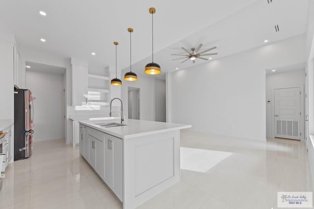 kitchen featuring a center island with sink, white cabinets, decorative light fixtures, light countertops, and a sink