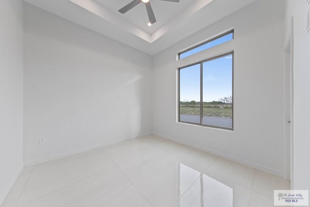 empty room featuring light tile patterned floors, ceiling fan, baseboards, and a raised ceiling