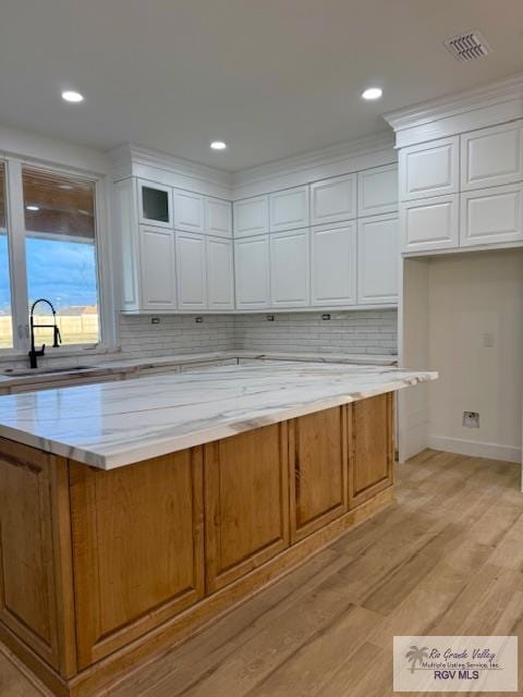 kitchen featuring sink, light hardwood / wood-style flooring, tasteful backsplash, light stone countertops, and white cabinets