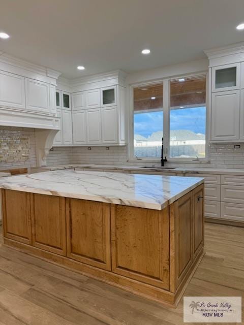 kitchen with a kitchen island, white cabinetry, sink, light stone counters, and light wood-type flooring