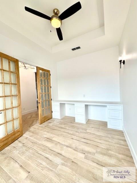 unfurnished office featuring french doors, ceiling fan, a raised ceiling, and light wood-type flooring