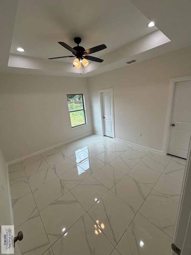 spare room with a tray ceiling and ceiling fan