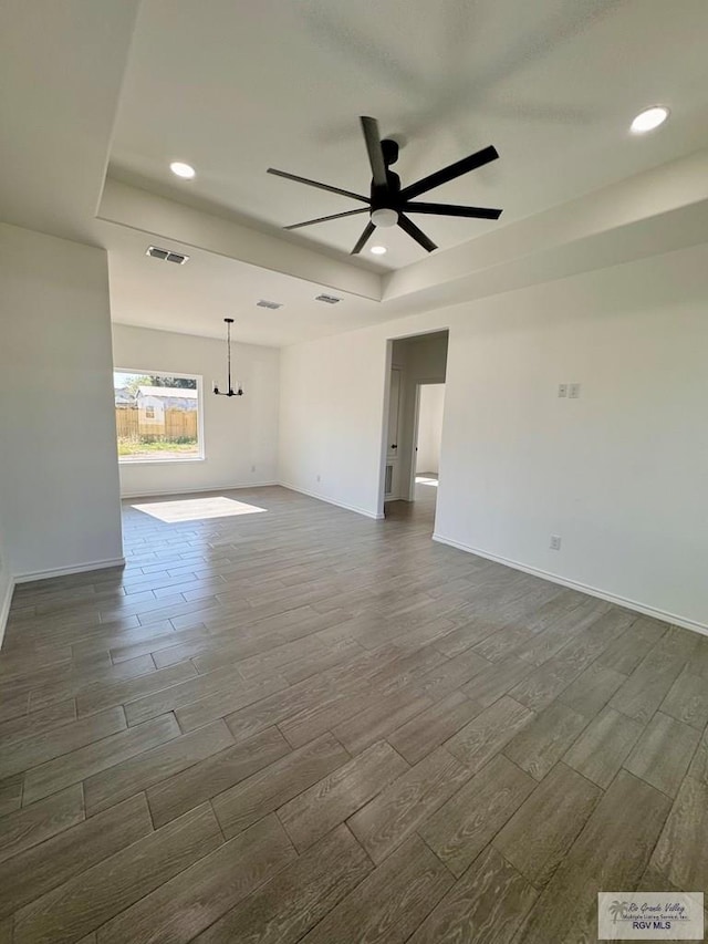 empty room with ceiling fan with notable chandelier and dark wood-type flooring