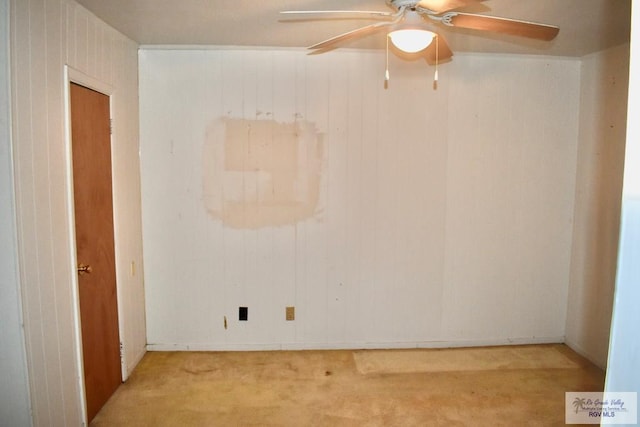 carpeted empty room with ceiling fan and wood walls