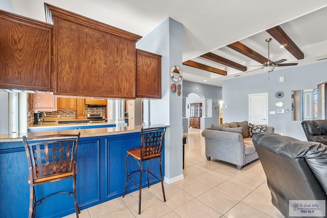 kitchen with beamed ceiling, a kitchen breakfast bar, decorative backsplash, light tile patterned floors, and ceiling fan