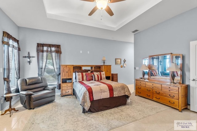 tiled bedroom featuring ceiling fan and a tray ceiling