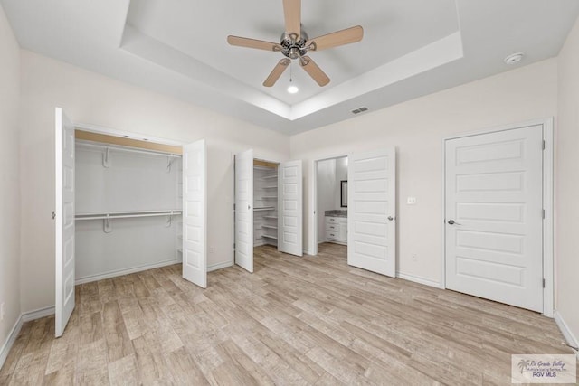 unfurnished bedroom with light hardwood / wood-style flooring, a raised ceiling, and ceiling fan