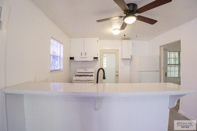 kitchen with light hardwood / wood-style flooring, range hood, kitchen peninsula, white appliances, and white cabinets