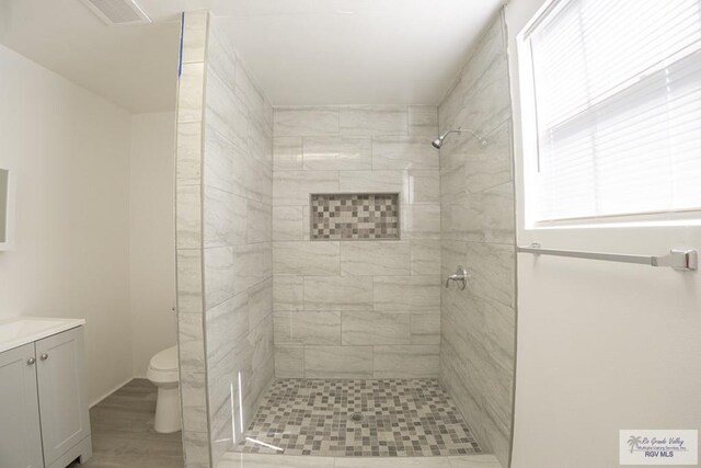 bathroom with tiled shower, vanity, and toilet