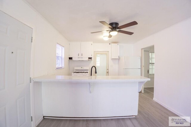 kitchen with white appliances, exhaust hood, kitchen peninsula, light hardwood / wood-style floors, and white cabinetry