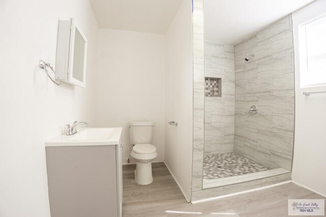 bathroom featuring tiled shower, hardwood / wood-style floors, vanity, and toilet