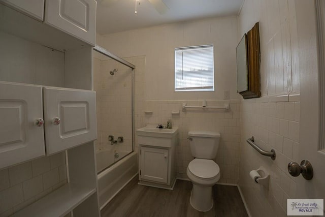 full bathroom with vanity, bath / shower combo with glass door, toilet, tile walls, and wood-type flooring