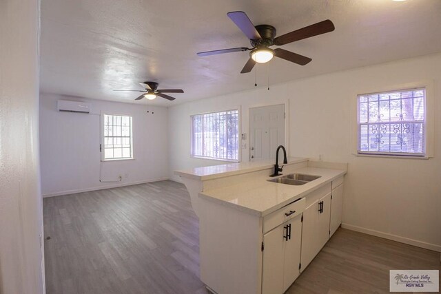 kitchen featuring an AC wall unit, kitchen peninsula, sink, and white cabinets