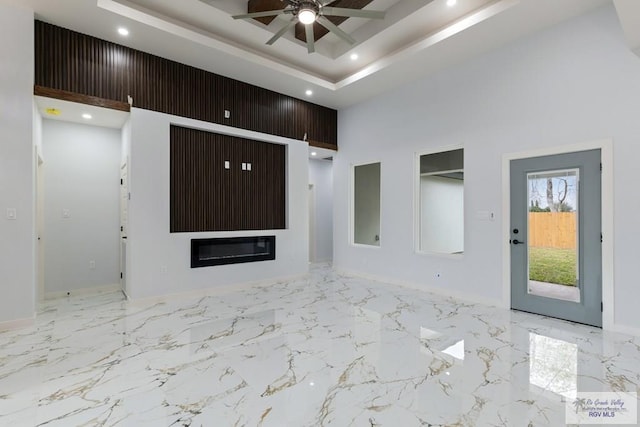 unfurnished living room with recessed lighting, a high ceiling, a ceiling fan, marble finish floor, and a tray ceiling