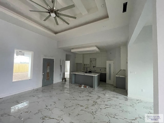 interior space with a towering ceiling, sink, ceiling fan, and a tray ceiling