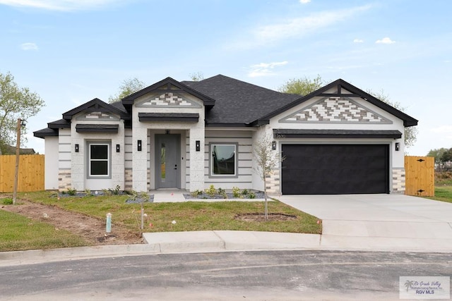 view of front of property featuring roof with shingles, concrete driveway, an attached garage, fence, and stone siding