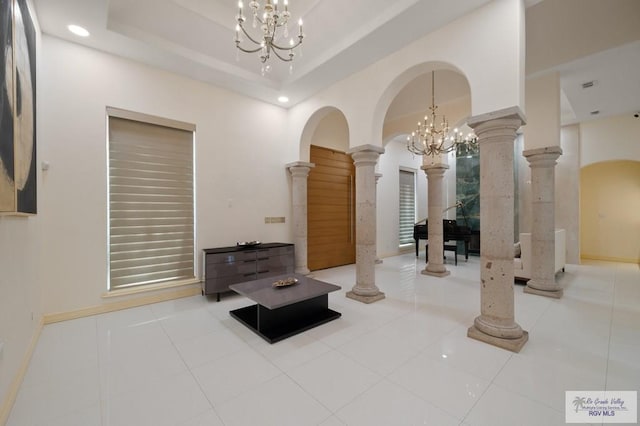 tiled living room featuring a tray ceiling, ornate columns, and a notable chandelier