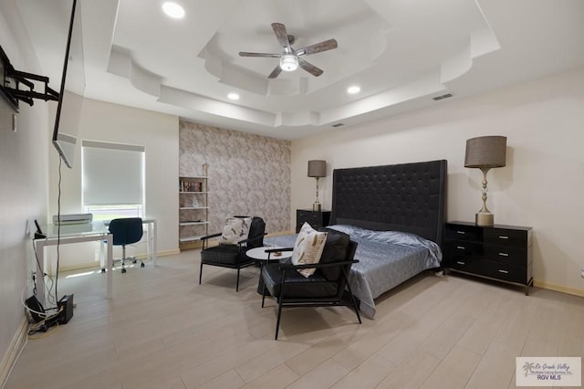 bedroom with ceiling fan, light hardwood / wood-style flooring, and a tray ceiling