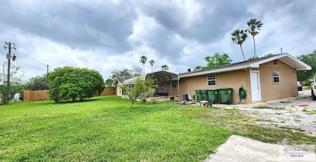 rear view of property with a detached carport, stucco siding, fence, and a yard