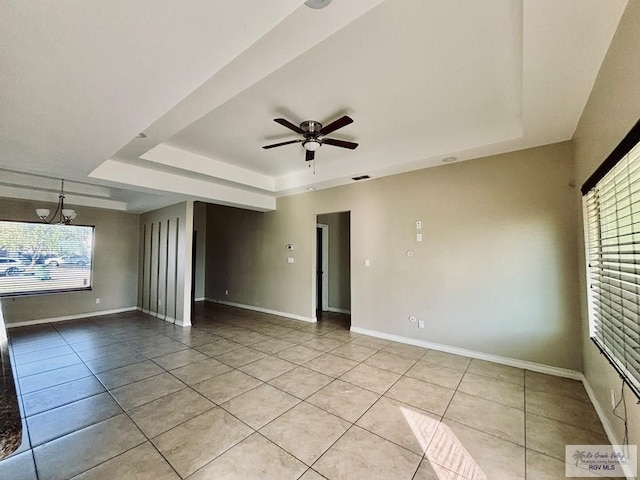 tiled spare room with a tray ceiling, plenty of natural light, and ceiling fan with notable chandelier