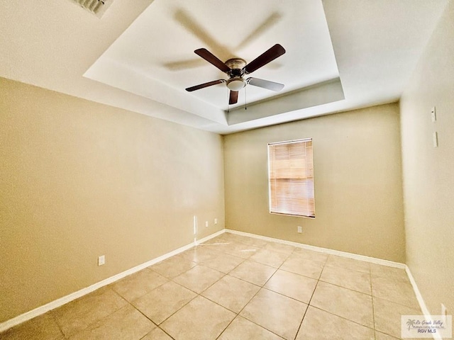 unfurnished room featuring a raised ceiling, ceiling fan, and light tile patterned flooring