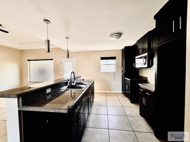 kitchen with sink, hanging light fixtures, dark stone countertops, a kitchen island with sink, and light tile patterned floors