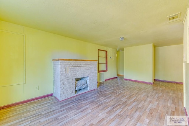 22916 N Oscar St, Harlingen, TX 78552 - unfurnished living room with light wood-style floors, a brick fireplace, and a textured ceiling