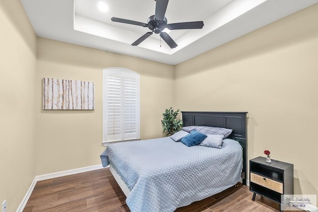 bedroom with a tray ceiling, ceiling fan, and dark hardwood / wood-style flooring