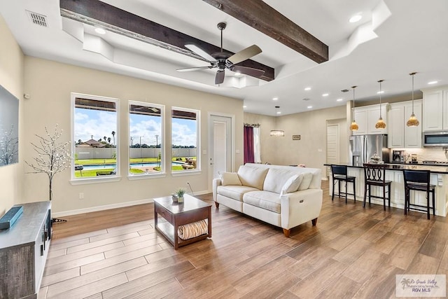 living room featuring ceiling fan, hardwood / wood-style floors, and beamed ceiling