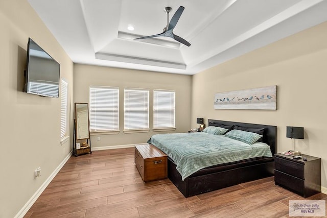 bedroom featuring ceiling fan, a raised ceiling, and light hardwood / wood-style flooring