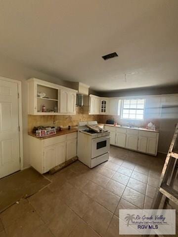 1022 Madison Ave, Harlingen, TX 78550 - kitchen with white gas stove, white cabinetry, tile patterned flooring, glass insert cabinets, and backsplash