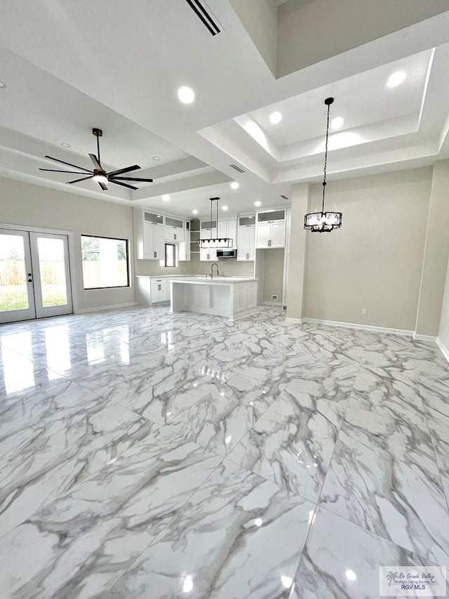 unfurnished living room with ceiling fan, a raised ceiling, sink, and french doors