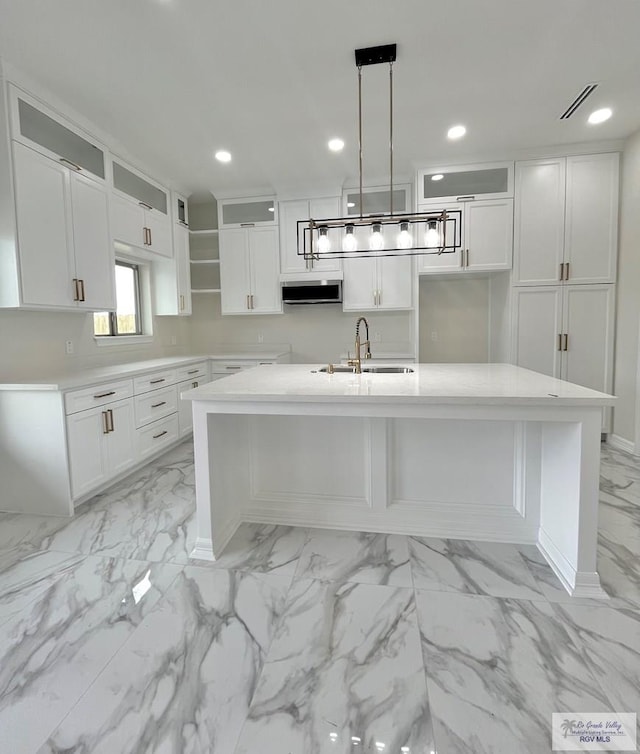 kitchen with white cabinetry, sink, extractor fan, decorative light fixtures, and a center island with sink