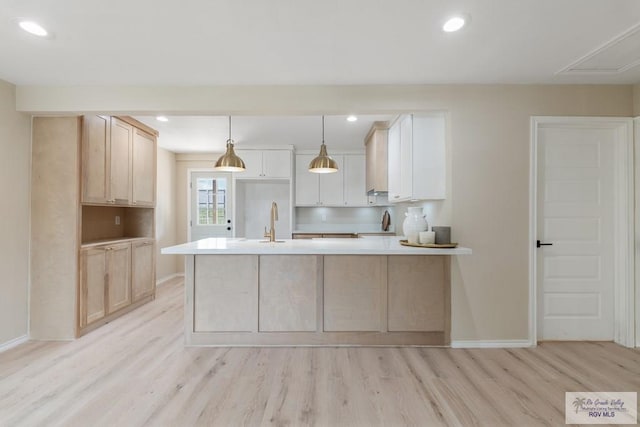 kitchen featuring sink, hanging light fixtures, light hardwood / wood-style floors, a center island with sink, and white cabinets