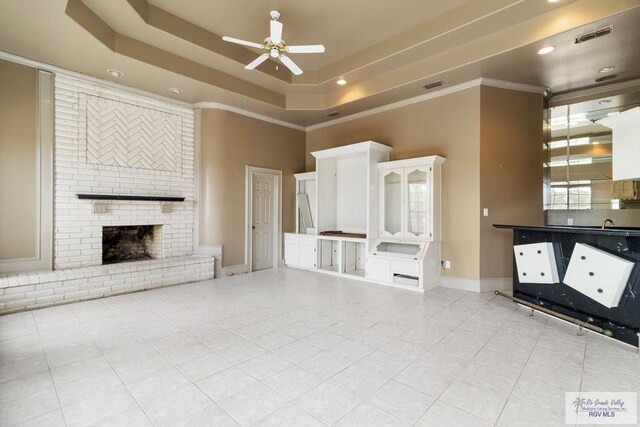 2107 S Victoria Rd, Donna, TX 78537 - unfurnished living room featuring ornamental molding, tile patterned floors, a brick fireplace, a tray ceiling, and ceiling fan