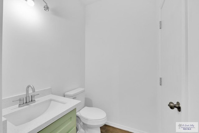 half bath featuring toilet, wood finished floors, vanity, and baseboards