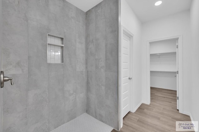 bathroom featuring tiled shower, a spacious closet, baseboards, and wood finished floors