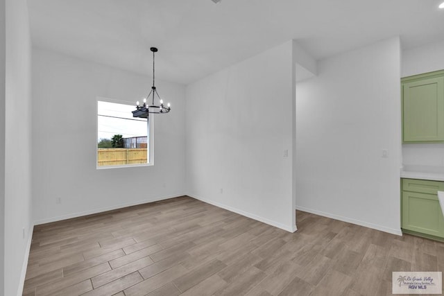 unfurnished dining area featuring a chandelier, light wood-type flooring, and baseboards