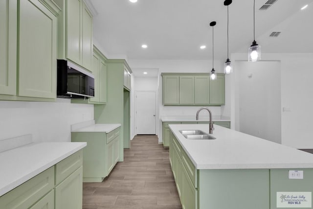 kitchen featuring a sink, visible vents, light countertops, an island with sink, and green cabinetry