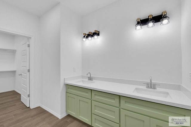 bathroom featuring wood finished floors, a sink, baseboards, and double vanity