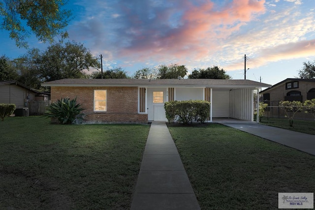 ranch-style home with driveway, fence, a front yard, central AC, and brick siding