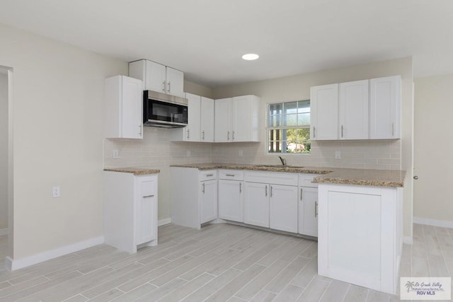 kitchen featuring tasteful backsplash, stainless steel microwave, light stone counters, and a sink