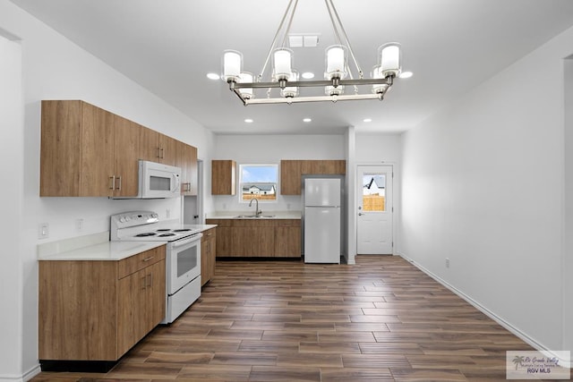 kitchen with white appliances, dark wood-type flooring, an inviting chandelier, sink, and hanging light fixtures