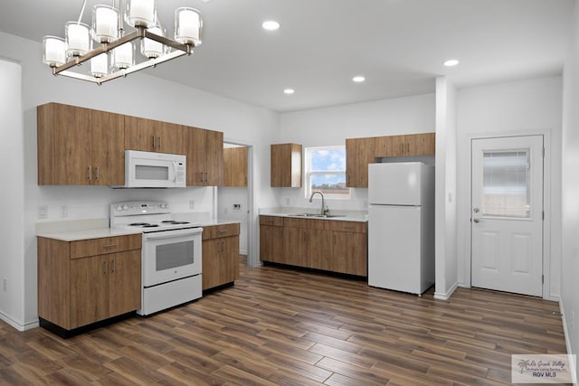 kitchen with sink, dark wood-type flooring, hanging light fixtures, an inviting chandelier, and white appliances