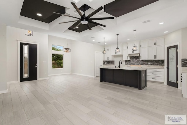 kitchen featuring white cabinetry, ceiling fan with notable chandelier, a center island with sink, and sink