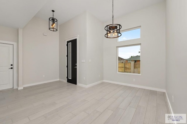 spare room with a notable chandelier, a high ceiling, and light hardwood / wood-style flooring